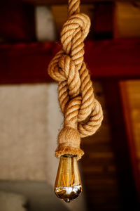 Close-up of rope tied on wooden post against wall with a lightbulb on the end