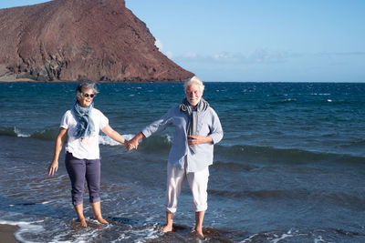 Portrait of senior man holding hands with woman while standing at shore against sky