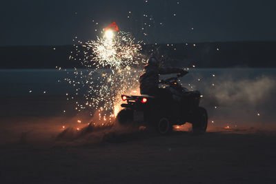 Athlete on a quad bike rides at night on a sandy beach with fireworks