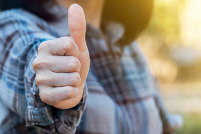 Midsection of woman gesturing thumbs up standing outdoors