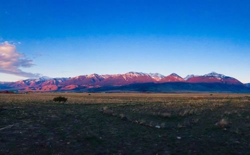 Scenic view of field and mountains against blue sky