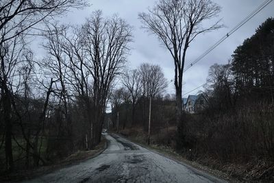 Empty road amidst bare trees against sky