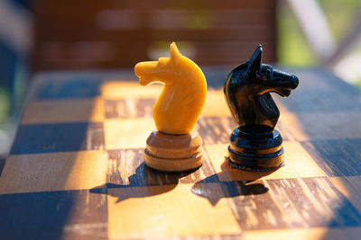 Two pieces of a chess knight, white and black, on an old chessboard.