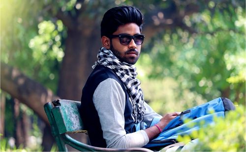 Portrait of young man wearing sunglasses while sitting on park bench