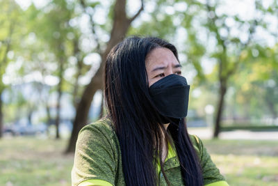 Depressed asian middle-aged woman wearing a medical face mask sitting in the park outdoors. 