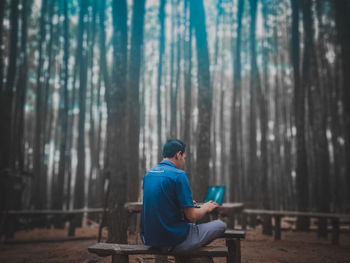 Side view of young man sitting on land in forest