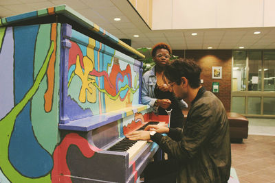 Woman standing by man playing piano