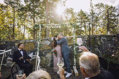 Newlywed couple kissing in front of guests raising toasts and minister with disability at wedding ceremony
