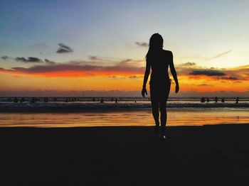 Silhouette woman walking on shore at beach against sky during sunset