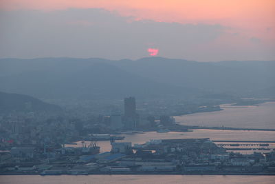 Cityscape by sea against sky during sunset