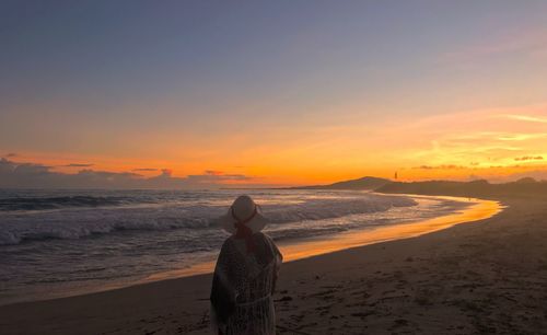 Rear view of woman standing on beach at sunset