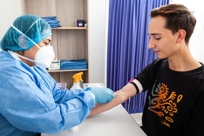 Young female nurse collecting a blood sample from a male patient in a clinic