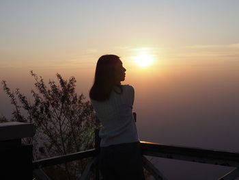 Silhouette person standing by railing against sky during sunset