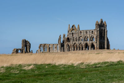 Old ruins on field against clear blue sky