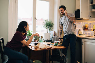 Woman looking at man talking on mobile phone in kitchen