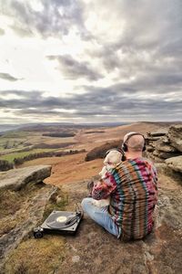 Man with dog listening music on land against cloudy sky