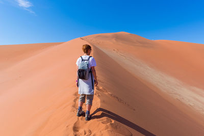 Rear view of woman walking on sand dune
