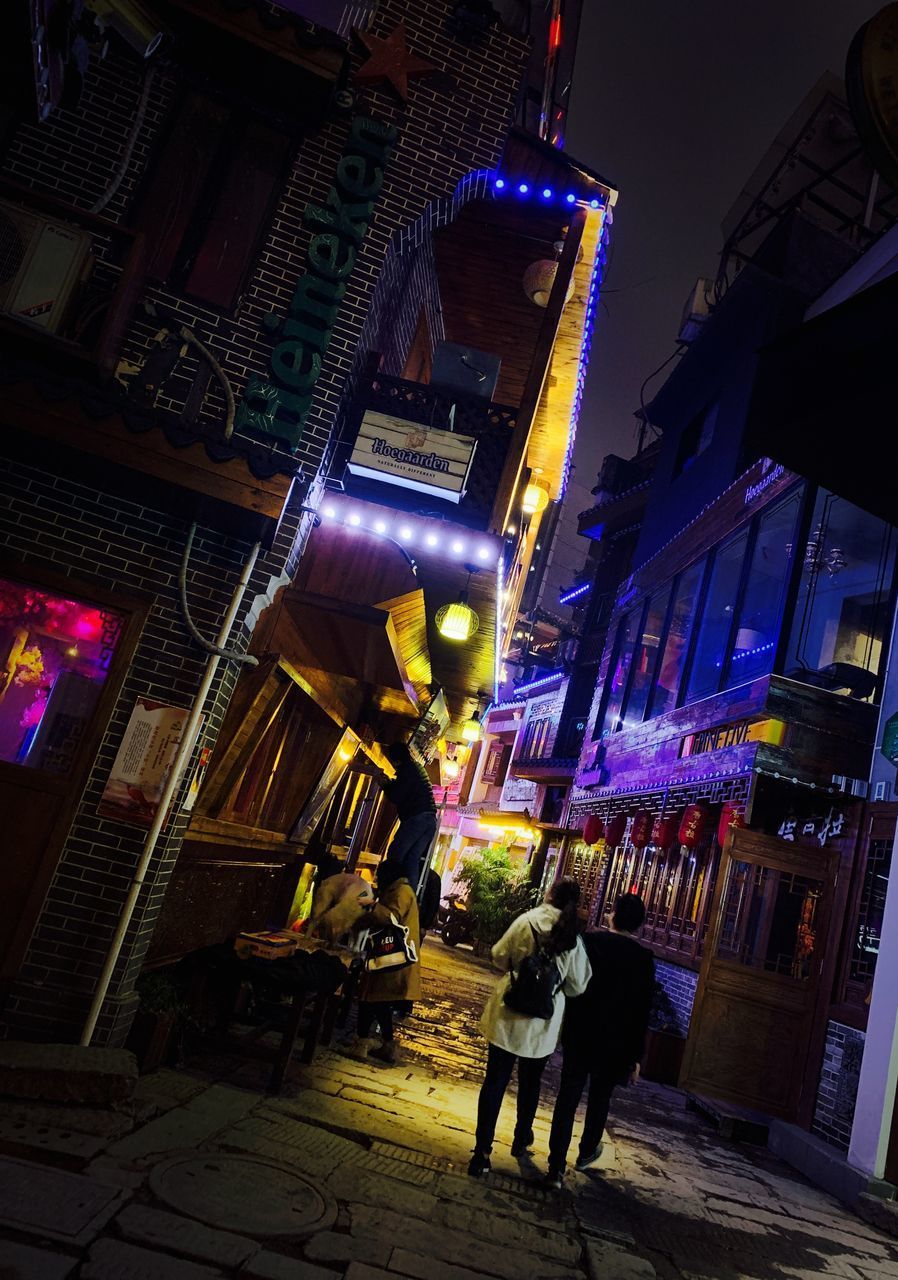 PEOPLE AT ILLUMINATED CITY BUILDINGS AT NIGHT