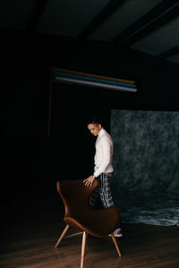 Side view of young man sitting on chair at home