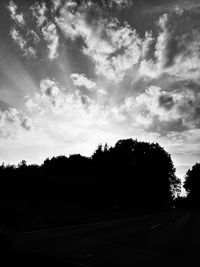 Silhouette trees by road against sky during sunset