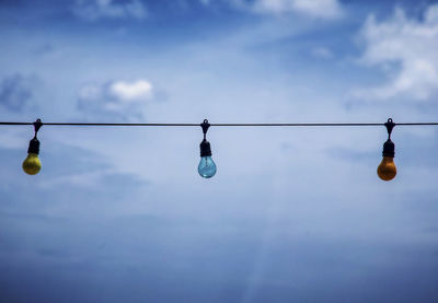 Low angle view of light bulbs hanging against sky