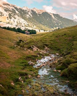 Scenic view of stream by mountains against sky