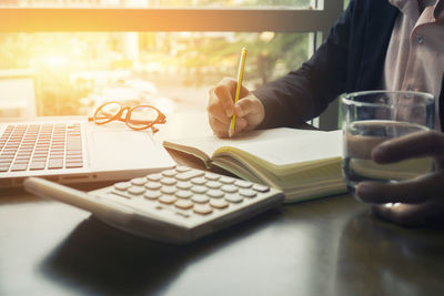 Midsection of businessman writing on book at office