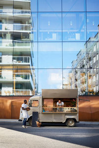 Multi-ethnic male owners at food truck parked on city street against glass building