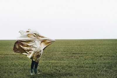 Person covering with foil standing on field against clear sky