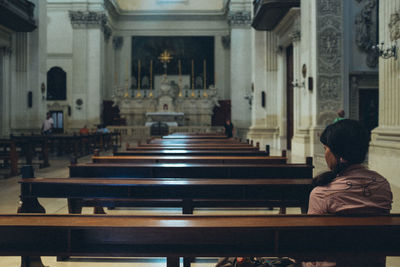 Rear view of man sitting on bench in building