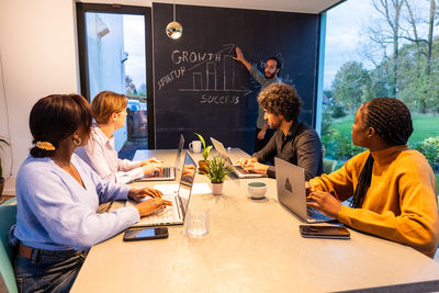 Side view of friends using digital tablet while sitting on table