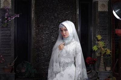 Portrait of bride wearing traditional clothing standing against wall