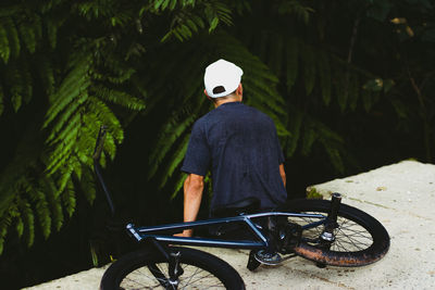 Rear view of man with bicycle sitting outdoors