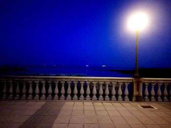 Illuminated street lights by sea against clear blue sky at night