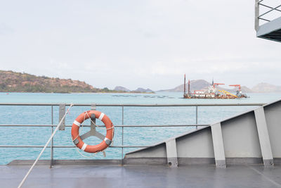 Man relaxing on railing by sea against sky