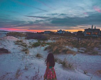 Girl standing at beach against sky during sunset