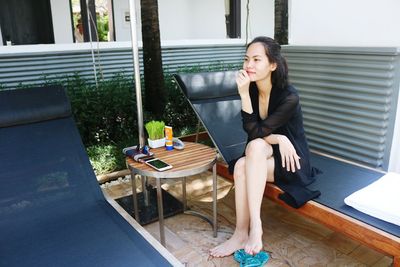 Young woman looking away while sitting on lounge chair