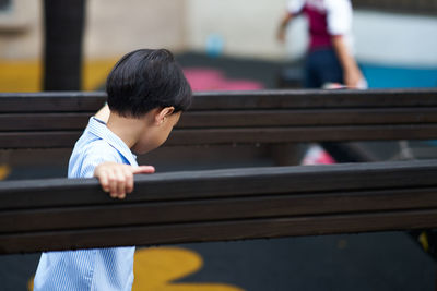Boy looking down while sitting on bar playground 