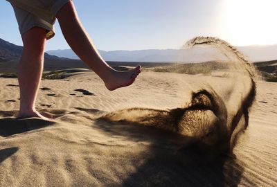 Low section of person on sand at beach against sky