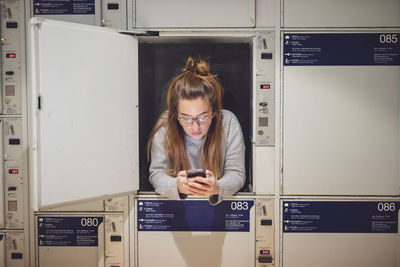 Young woman using phone in locker