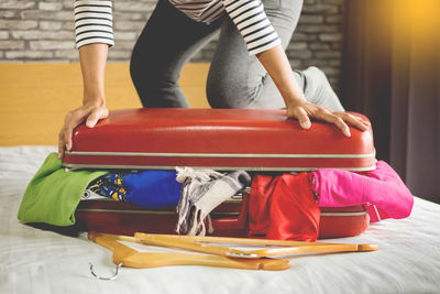 Midsection of woman packing suitcase on bed at home