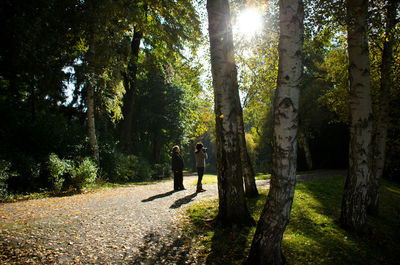 Women standing on footpath amidst trees at park