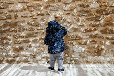 Rear view of baby girl wearing warm clothing while standing by wall