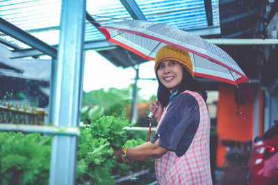 Portrait of smiling young woman with umbrella standing in greenhouse