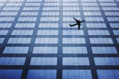 Reflection of airplane on glass building in city