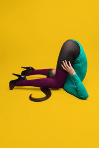 Young woman exercising against yellow background