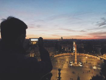 Rear view of man looking at cityscape against sky during sunset