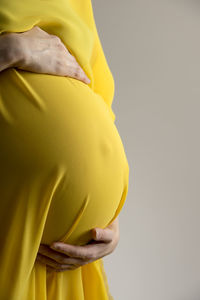 Close-up of woman holding yellow while standing against gray background