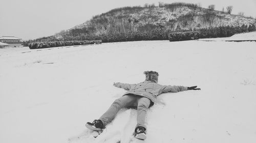 Full length person lying on snow covered field by mountain against sky