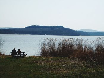 People sitting on golf course by lake against sky